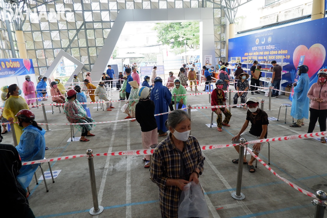 People lining up two meter apart to wait for their turn in front of the rice dispenser at the Binh Thuan Ward Cultural House