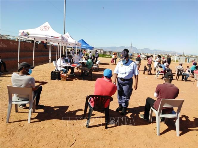 Cảnh sát nhắc nhở người dân thực hiện giãn cách xã hội trong khi chờ đợi đến lượt tại một điểm xét nghiệm Covid-19. Ảnh: Phi Hùng - PV TTXVN tại Nam Phi