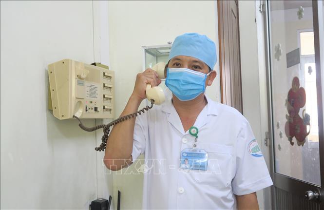 Bác sỹ Nguyễn Thanh Phong, Trưởng Khoa Nhiễm D- Bệnh viện Bệnh Nhiệt đới Thành phố Hồ Chí Minh trao đổi bằng điện thoại với bệnh nhân trong phòng cách ly áp lực âm. Ảnh: Đinh Hằng/ TTXVN