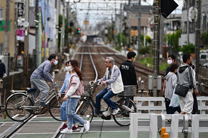  Người dân đi xe đạp qua đường ray tàu hỏa tại Tokyo, Nhật Bản, ngày 4/5/2020. Ảnh: AFP/ TTXVN