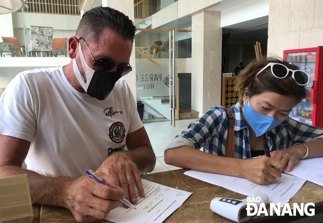 Tourists filling in health forms under the guidance of hotel receptionists 