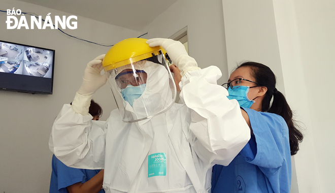 Nhân viên y tế Bệnh viện Đà Nẵng hỗ trợ đồng nghiệp mang trang phục bảo hộ trước khi vào khu điều trị bệnh nhân Covid-19.  Ảnh: PHAN CHUNG	