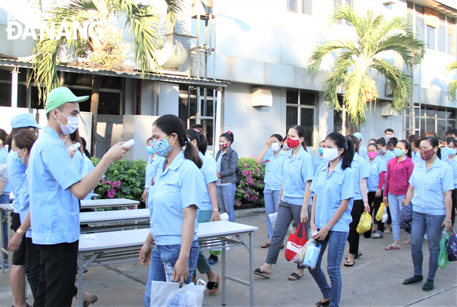 Workers at a company wearing face masks queue in lines to have their body temperatures measured before entering the workplace