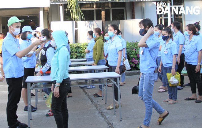 Workers at a company wearing face coverings are queued for having their body temperatures measured before entering their workplace