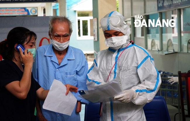 Nhân viên y tế Bệnh viện dã chiến Hòa Vang hỗ trợ bệnh nhân cao tuổi, hướng dẫn các biện pháp theo dõi sức khỏe tại nhà sau khi xuất viện. Ảnh: PHAN CHUNG
