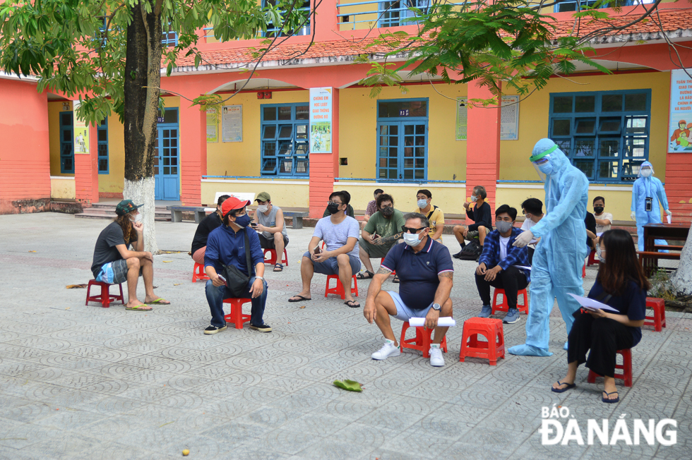 Foreigners sitting far apart and wearing  face coverings while waiting to be tested for Covid-19 in Nai Hien Dong Ward 