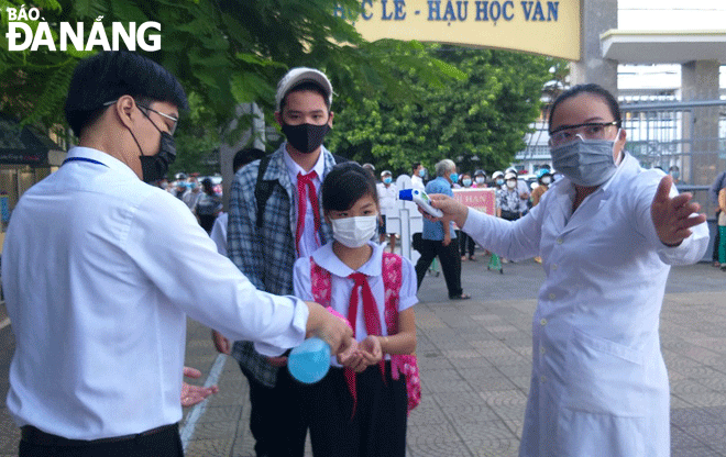 Học sinh Trường THCS Nguyễn Huệ được giáo viên đo thân nhiệt và sát khuẩn trước khi vào lớp học. Ảnh: NGỌC PHÚ	
