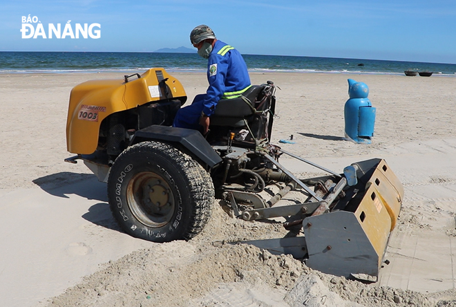 Công nhân Xí nghiệp Môi trường sông biển dùng máy sàng cát để thu dọn những mảnh rác nhỏ trong cát. Ảnh: VĂN HOÀNG