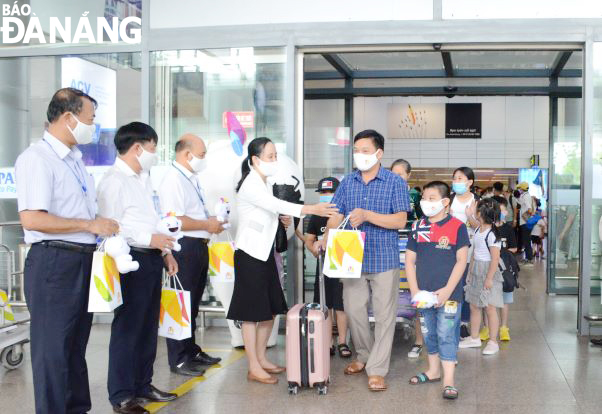 Những vị khách đầu tiên của đoàn 55 khách đặt chân đến sân bay Đà Nẵng và nhận quà của đại diện ngành du lịch thành phố. Ảnh: THU HÀ.