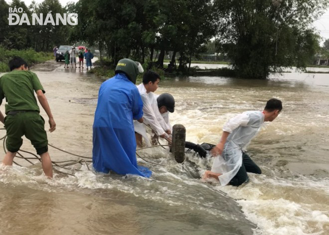 Lực lượng chức năng xã Hòa Phong kịp thời cứu vớt một người đi xe máy đi qua đoạn đường ngập lũ, nước chảy xiết cuốn trôi. Ảnh: HOÀNG HIỆP