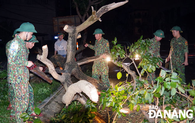 Cán bộ, chiến sĩ Biên phòng cửa khẩu cảng Đà Nẵng cưa cắt các cây lớn bị ngã đổ chắn ngang các tuyến đường. (Ảnh dưới, bên trái) 					  Ảnh: XUÂN SƠN
