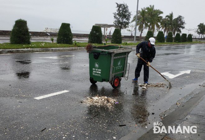 Công nhân của Công ty CP Môi trường Đô thị Đà Nẵng thu dọn cát, rác do sóng biển tấp trên mặt đường Nguyễn Tất Thành. Ảnh: HOÀNG HIỆP