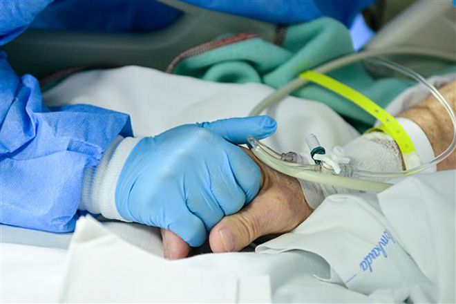  Nhân viên y tế nắm tay an ủi bênh nhân nhiễm Covid-19 tại bệnh viện ở Bergamo, Italy. Ảnh: AFP/TTXVN