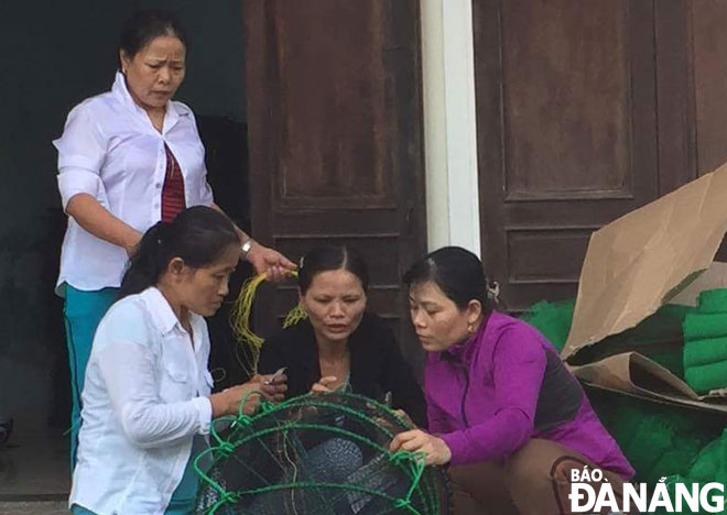 Chị Nguyễn Thị Cẩn, Tổ trưởng tổ đan lưới xuất khẩu (đứng) đang giao hàng cho hội viên đem về nhà đan. Ảnh: T.V	