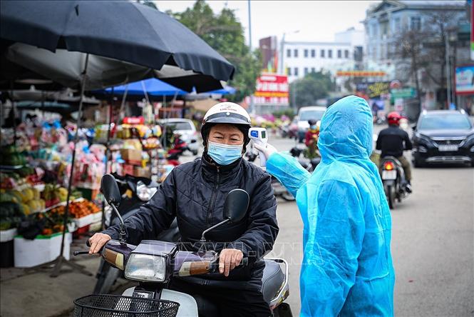 Đo thân nhiệt, sàng lọc triệu chứng COVID-19 cho người dân. Ảnh: TTXVN