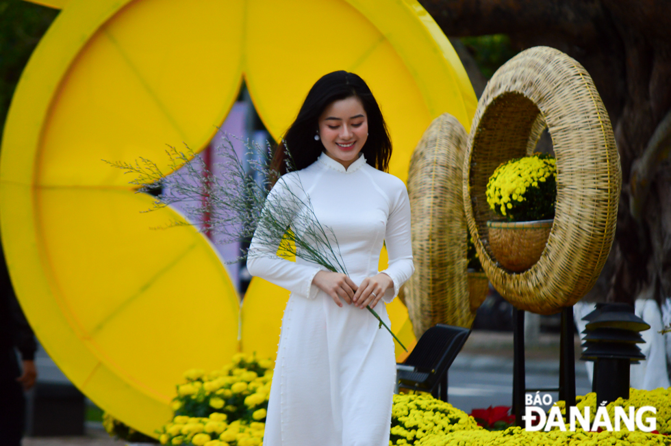 A beautiful lady wearing 'ao dai' (Vietnamese traditional long dress) posing for souvenir photos with colourful flowers