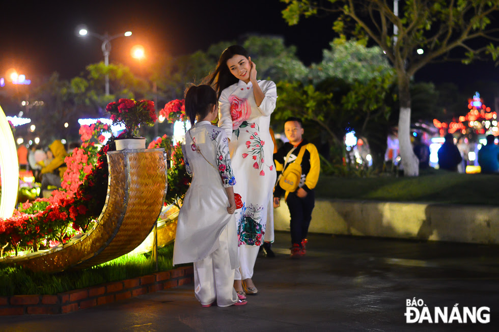 A girl and a woman wearing 'ao dai' (Vietnamese traditional long dress) posing for souvenir photos with colourful flowers