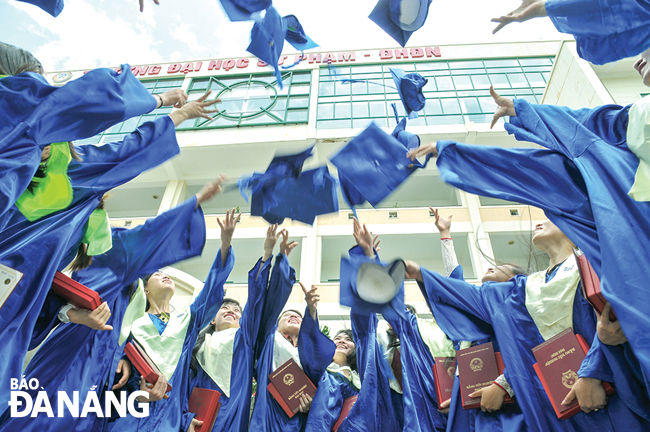 A group of students from the Da Nang University of Education celebrating their graduation day outdoors while throwing their caps up in the air