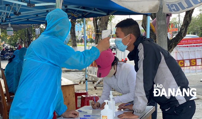  A Youth Union member from Ngu Hanh Son District measuring the body temperature of an arrivak in the city at a checkpoint on Tran Dai Nghia Street