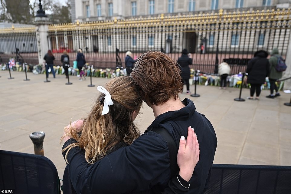 Một cặp đôi chứng kiến mọi người đặt hoa tưởng nhớ Hoàng thân Philip bên ngoài Cung điện Buckingham. Ảnh: EPA