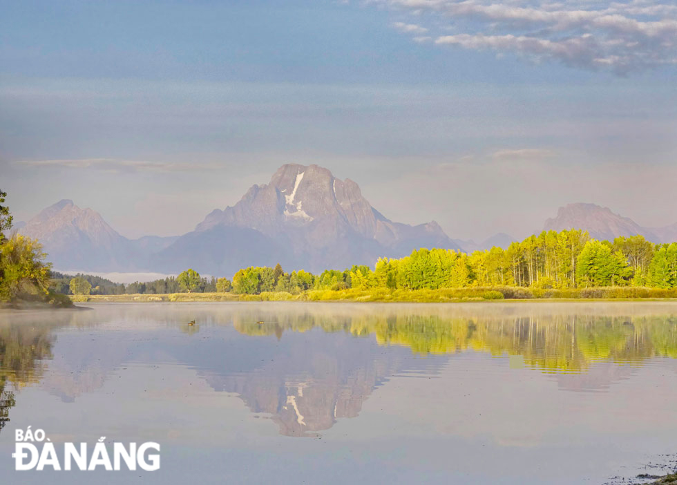 Beautiful Snake River with stunning reflections of Mount Moran and a golden autumn forest in the glimmering rays of sunlight shining the ground at the Grand Teton National Park, Wyoming State.