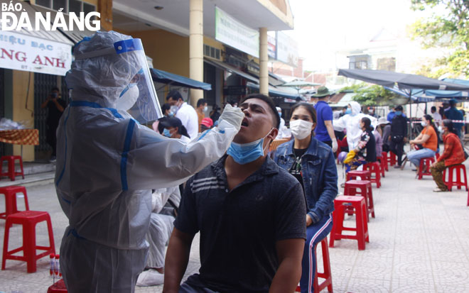 A medical worker collecting a throat and nose swab from a stall holder at the Phuoc My Market 