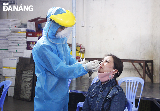 A medical worker collecting  a combined throat and nose swab of a stall holder. Photo: XUAN DUNG
