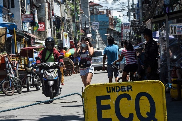 A policeman (right) monitors people at the entrance to a neighbourhood under strict quarantine measures in Pasay City, suburban Manila (Photo: AFP)