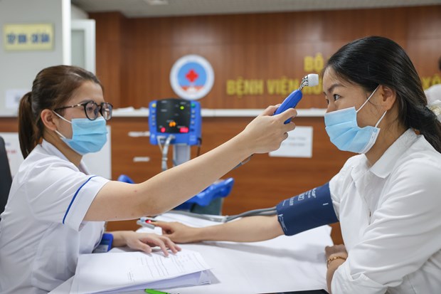 Đo nhiệt độ, huyết áp của người đi tiêm vaccine phòng Covid-19. (Ảnh: Minh Sơn/Vietnam+)