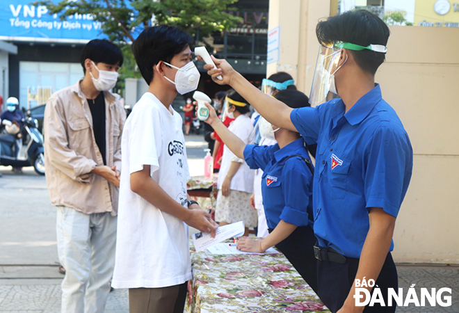 Lực lượng đoàn viên, thanh niên đo thân nhiệt cho thí sinh trước khi vào điểm thi lấy mẫu xét nghiệm SARS-CoV-2. (Ảnh chụp tại điểm thi Trường THPT Trần Phú). Ảnh: NGỌC HÀ
