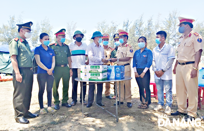 Anh Nguyễn Thành Hưng (thứ 5, từ trái sang) tặng quà cho lực lượng tuyến đầu chống dịch. (Ảnh chụp tháng 8-2020) 		                 Ảnh: THÀNH HƯNG