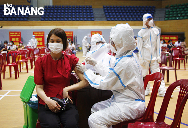 A healthcare professional wearing personal protective equipment giving a vaccine to an adult woman in a mask. Photo: XUAN DUNG
