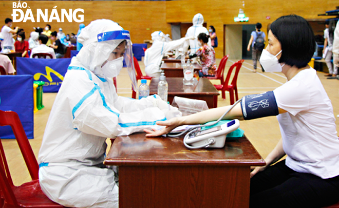 A medical staff measured the blood pressure of a woman before she get vaccinated against COVID-19 at the Tien Son Sports Arena on July 29. Photo: XUAN DUNG