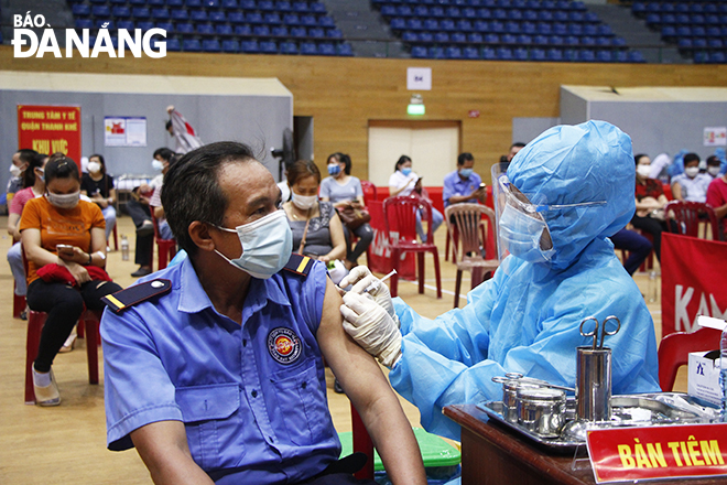 A healthcare professional wearing personal protective equipment giving a vaccine to a man in a mask. Photo: XUAN DUNG