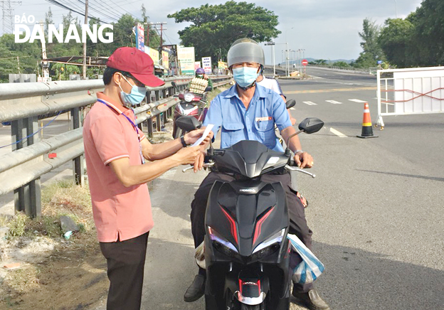 Teacher Dong Chi Huong (left) is seen checking travel permits shown by passersby at the Nam O bridge’s checkpoint. Photo: NGOC PHU