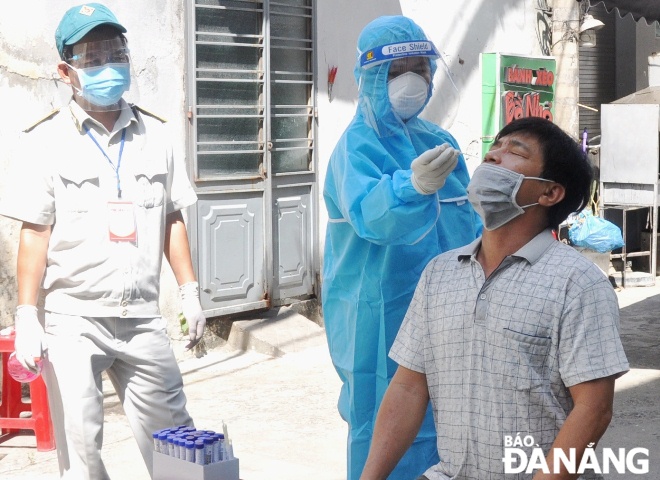 A healthcare worker is taking nasal swab of a household representative in the city to test for COVID-19. Photo: LE HUNG