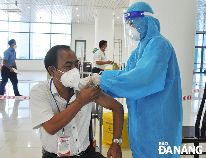 A healthcare professional in personal protective clothing giving a vaccinate against COVID-19 to an eligible man in mask. Photo: LE HUNG