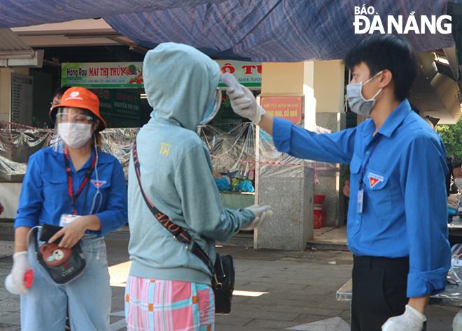  Before entering the market, all shoppers must have their body temperatures measured and their hand disinfected by the functional force. Photo: VAN HOANG