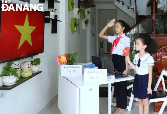 Pupils from the Nguyen Hue Junior High School and the Le Lai Primary School respectively salute the flag before their schools-held online ceremonies to welcome in the new academic year. Photo: NGOC HA.