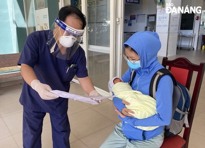 Lãnh đạo Trung tâm Y tế huyện Hòa Vang (trái) trao giấy xuất viện cho mẹ con bệnh nhân M. Ảnh: CTV