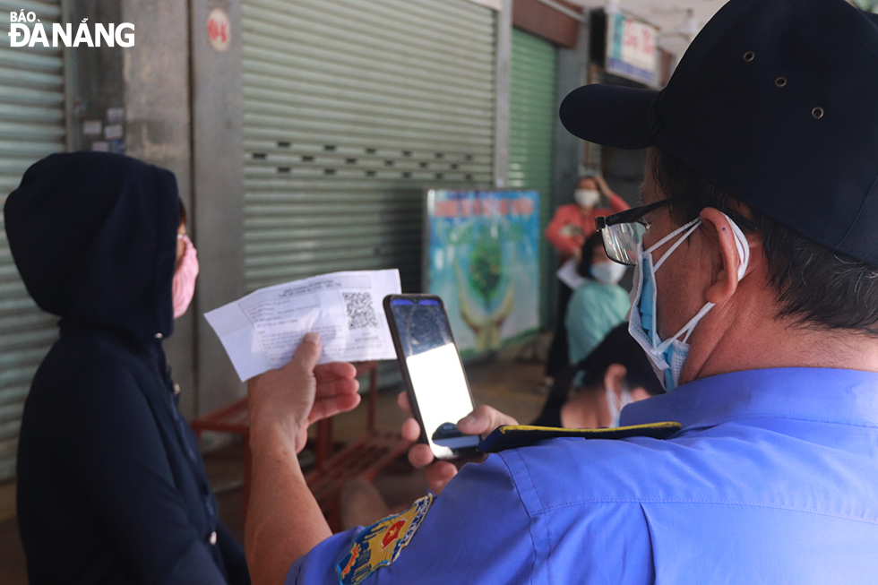 After re-opening the Han Maket in Hai Chau District, the authority of this market has arranged seats for patrons to keep a safe distance between them while waiting their turn to enter the market as only 5 people are allowed inside the market at one time in order to prevent the spread of the disease.  In the photo: Guards at the Han market checking QR code on entry card of a patron. Photo: DAC MANH