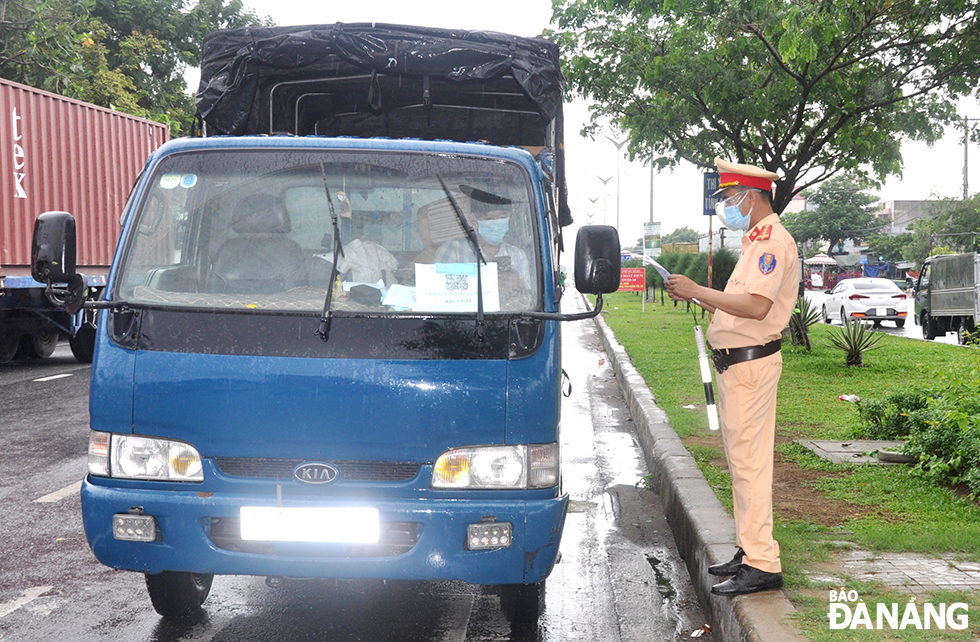  Traffic police on duty at a checkpoint on Tran Dai Nghia Street check a truck driver's travel pass.