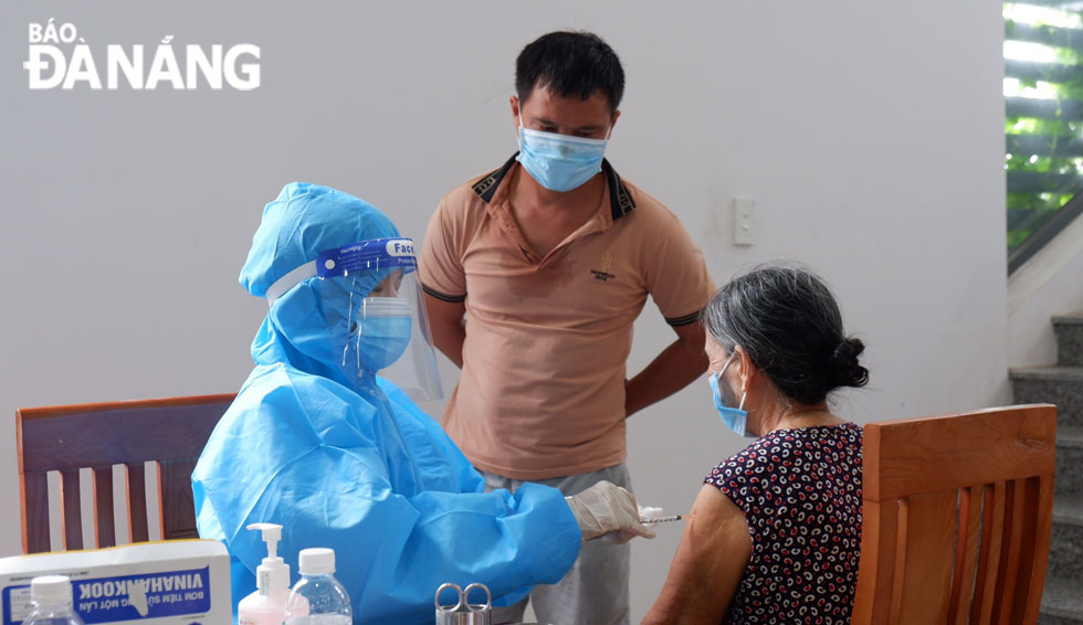 A healthcare professional administering COVID-19 vaccine for a senior woman in mask. Photo: PHAN CHUNG