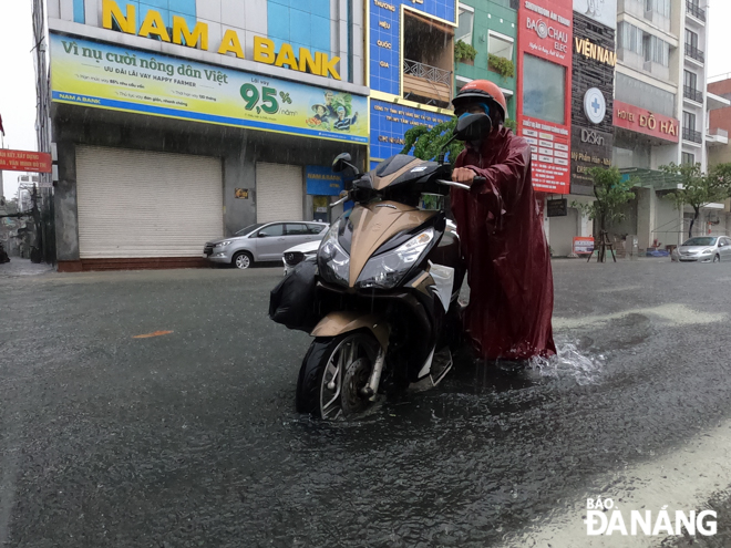 Many motorbike riders must walk through flooded streets because their vehicles stall in water and they find it difficult to drive under heavy rain. Photo: XUAN SON