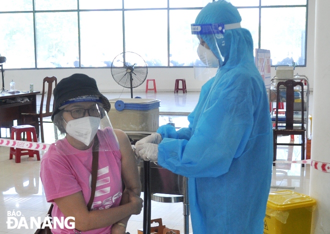 A healthcare profesional administering a Covid-19 vaccine to a woman in mask Photo: LE HUNG