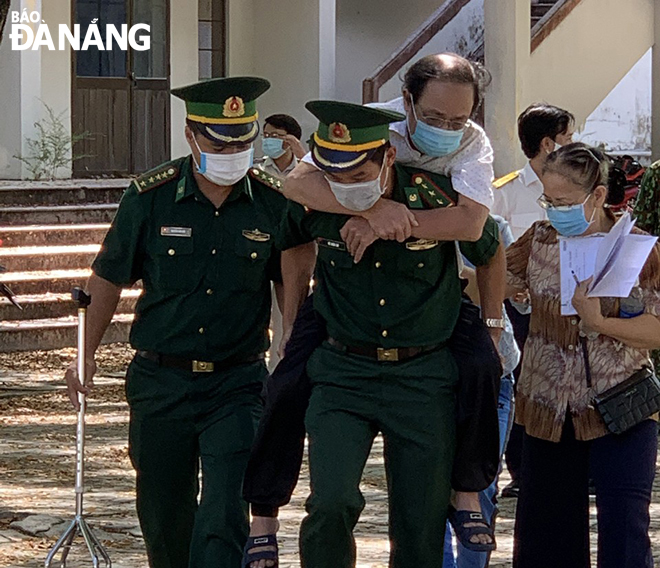 Cán bộ, chiến sĩ Biên phòng Đà Nẵng cõng người già đến nơi tiêm vắc-xin Covid-19 tại điểm tiêm chủng thuộc Trường THPT Phan Châu Trinh. Ảnh: HỒNG QUANG