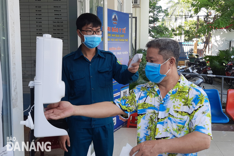 Local residents coming to the headquarters of the Nai Hien Dong Ward administration, Son Tra District, for the handling of administrative procedures must have their body temperatures checked and make medical declarations before entering administrative transaction sites here. Photo: TRONG HUY