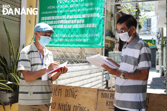 Ông Nguyễn Anh Tuấn (phải) trao đổi công việc với thành viên Tổ Covid-19 cộng đồng tại chốt kiểm soát vào kiệt 407 Lê Duẩn. Ảnh: TIỂU YẾN