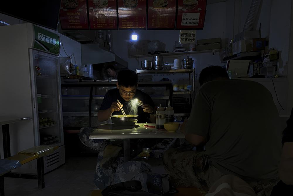 Một người đàn ông sử dụng điện thoại để chiếu đèn khi ăn mỳ trong lúc mất điện tại tỉnh Liêu Ninh, Trung Quốc. Ảnh: AP