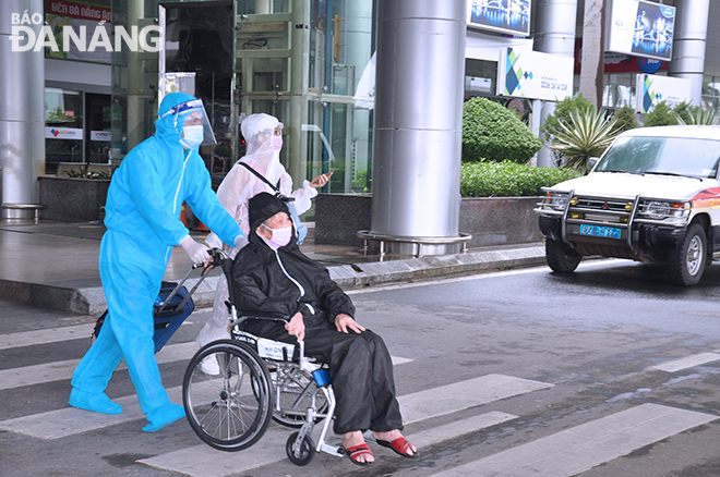 A ground staff pushing an older man in a wheelchair out of the airport. Photo: THANH LAN